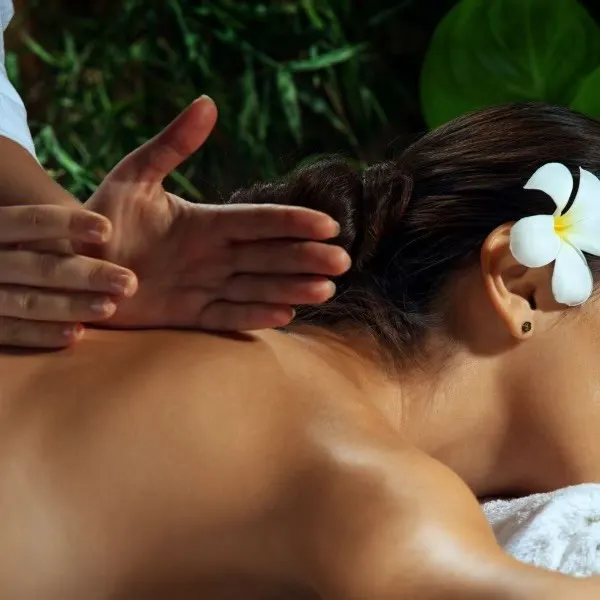 Guest with a frangipani in her hair receiving a back massage